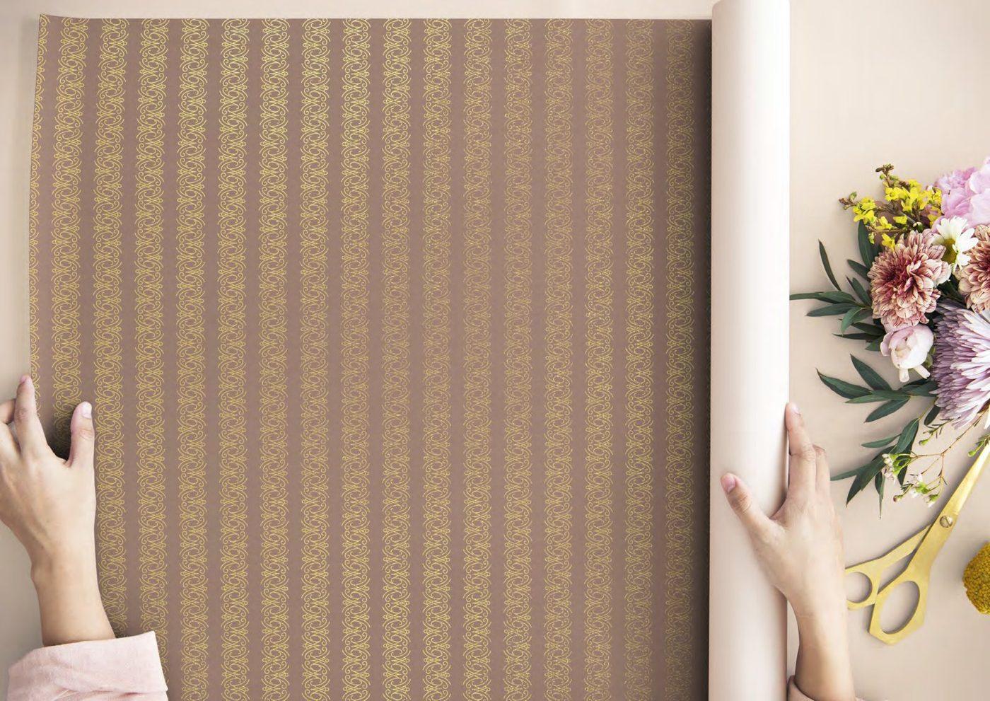 Hands unrolling a gold Marie-Antoinette patterned wallpaper
